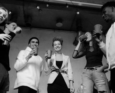 A group of diverse young adults enjoying a lively indoor party in black and white.
