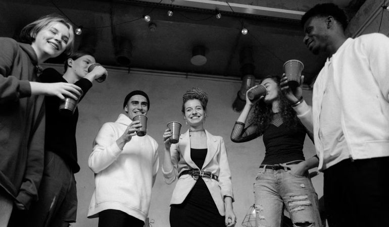 A group of diverse young adults enjoying a lively indoor party in black and white.
