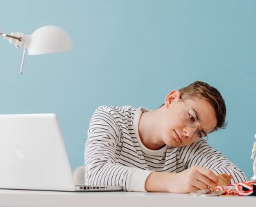 Teenager with eyeglasses contemplating medals at desk with laptop and trophies.